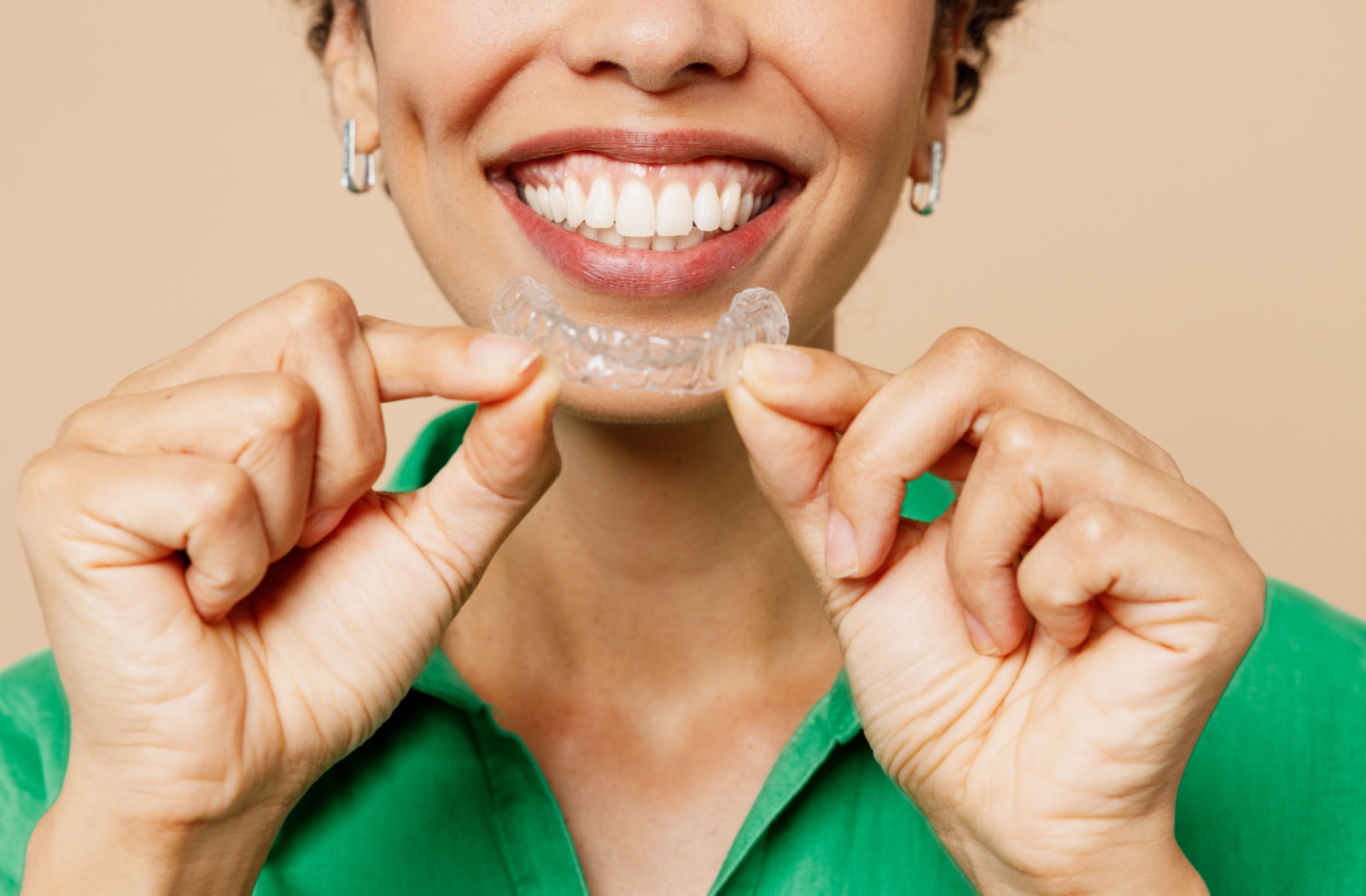 A person smiles while holding a clear Invisalign aligner in front of their teeth.