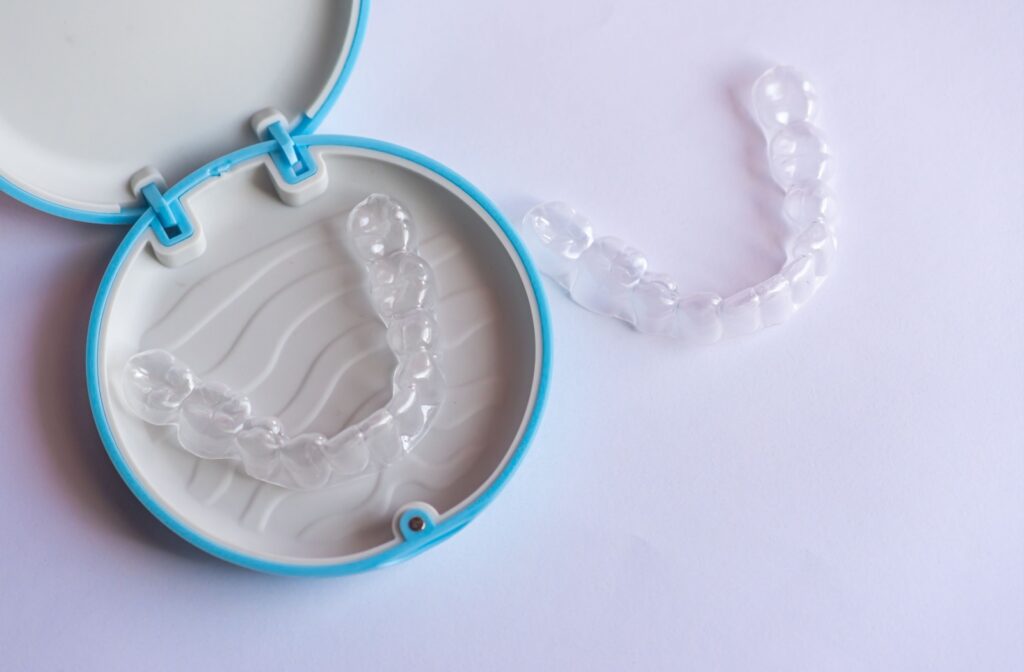 Two clear Invisalign aligners are shown, with one inside a blue storage case and one placed on a white surface.