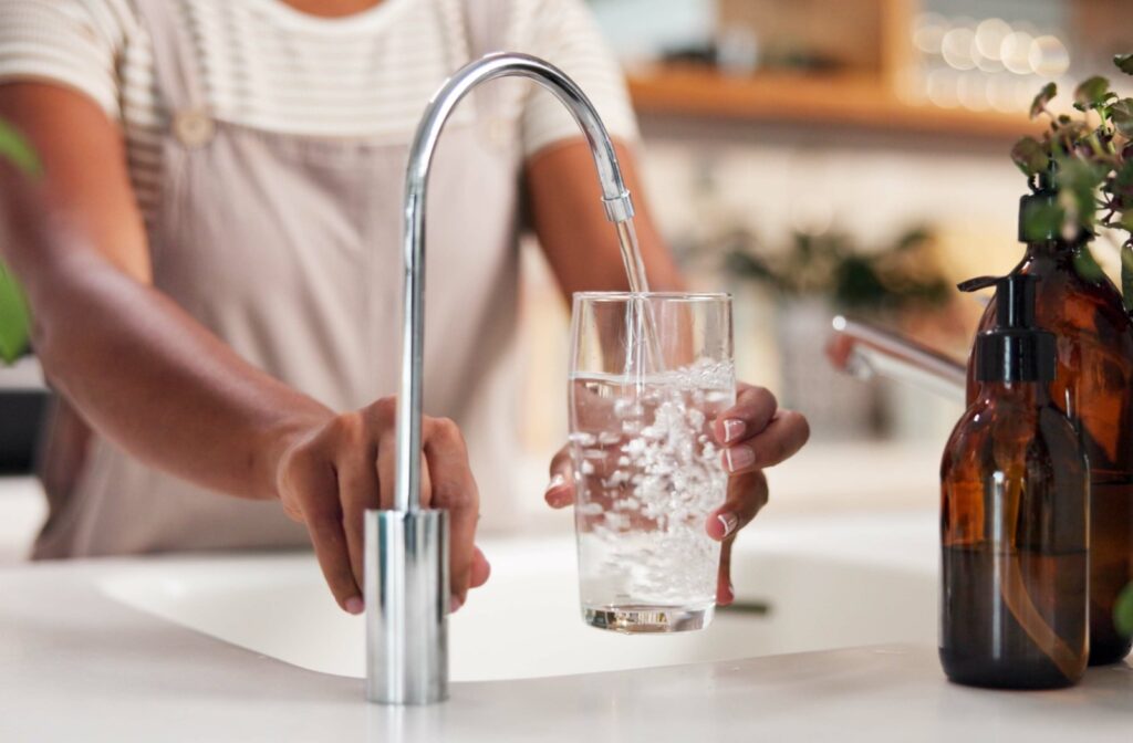A person using a kitchen sink to fill a cup full of water