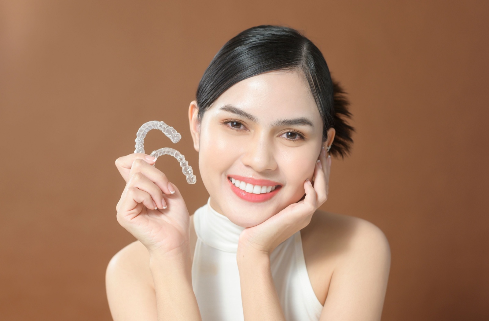 A model smiles while holding two invisalign trays in their hand